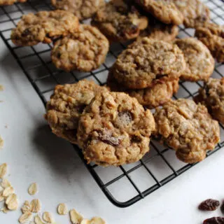oatmeal cinnamon drop cookies on cooling rack with oatmeal and raisins nearby.