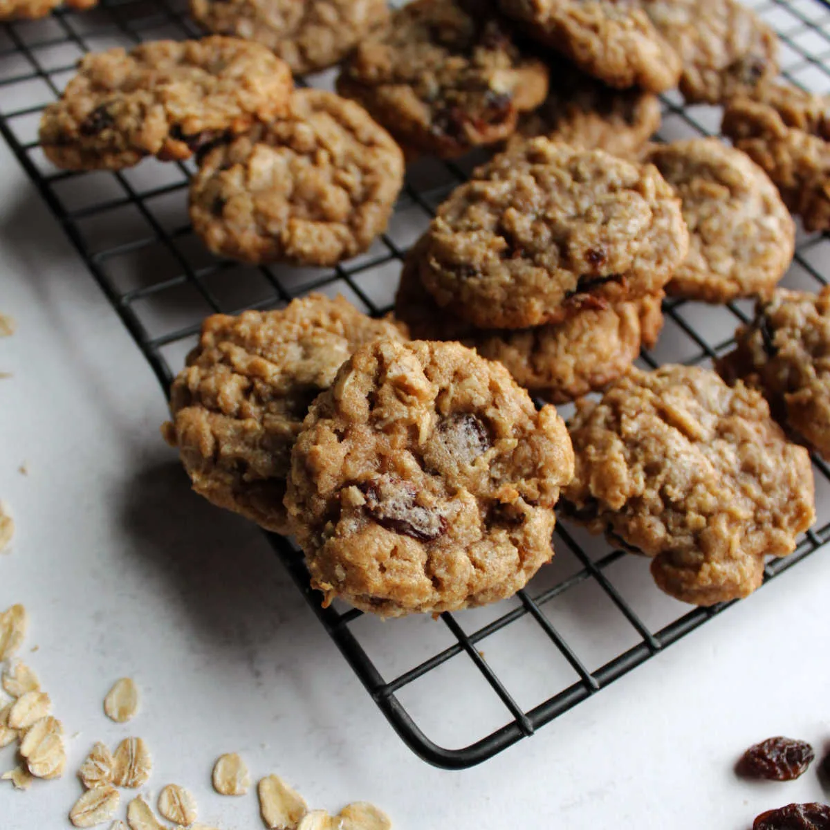 oatmeal cinnamon drop cookies on cooling rack with oatmeal and raisins nearby.