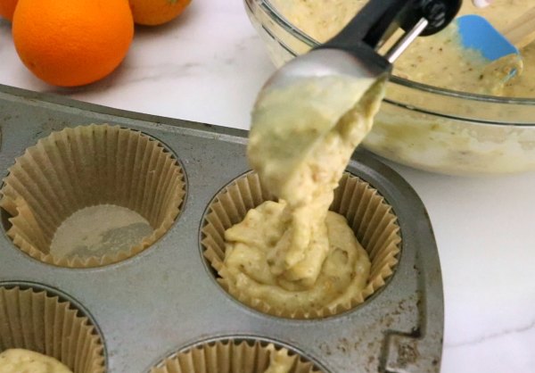 using ice cream scoop to transfer orange pistachio muffin batter into cupcake liners.