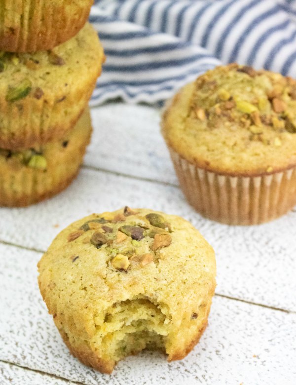 orange muffin with chopped pistachios on top with bite missing