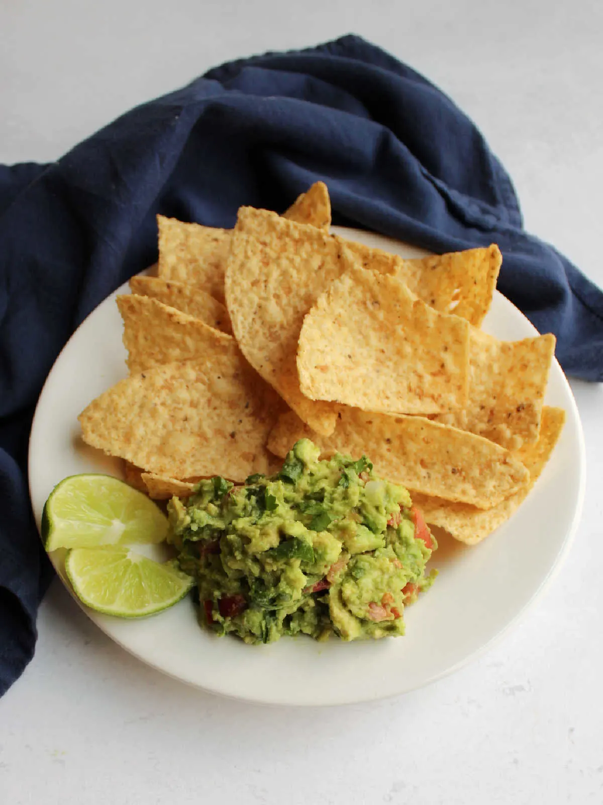 Plate of chunky homemade guacamole served with two lime wedges and tortilla chips.