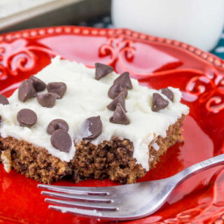 Piece of chocolate chip cookie dough Texas sheet cake with bite missing on red plate with fork.