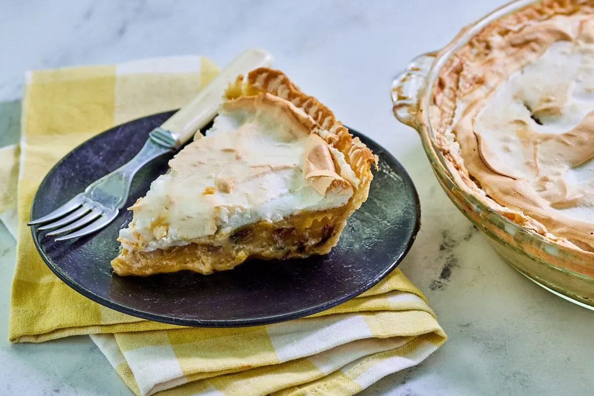 Piece of sour cream raisin pie showing thick custard filling, and fluffy white meringue with golden brown top, ready to eat.