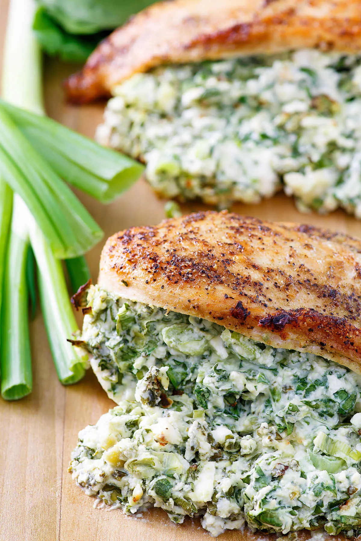 close up of chicken breasts over stuffed with creamy spinach and feta cheese mixture with green onions nearby.
