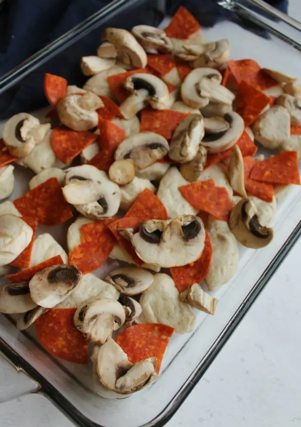 biscuits with pepperoni and mushrooms in pan ready to turn into pizza casserole bake.