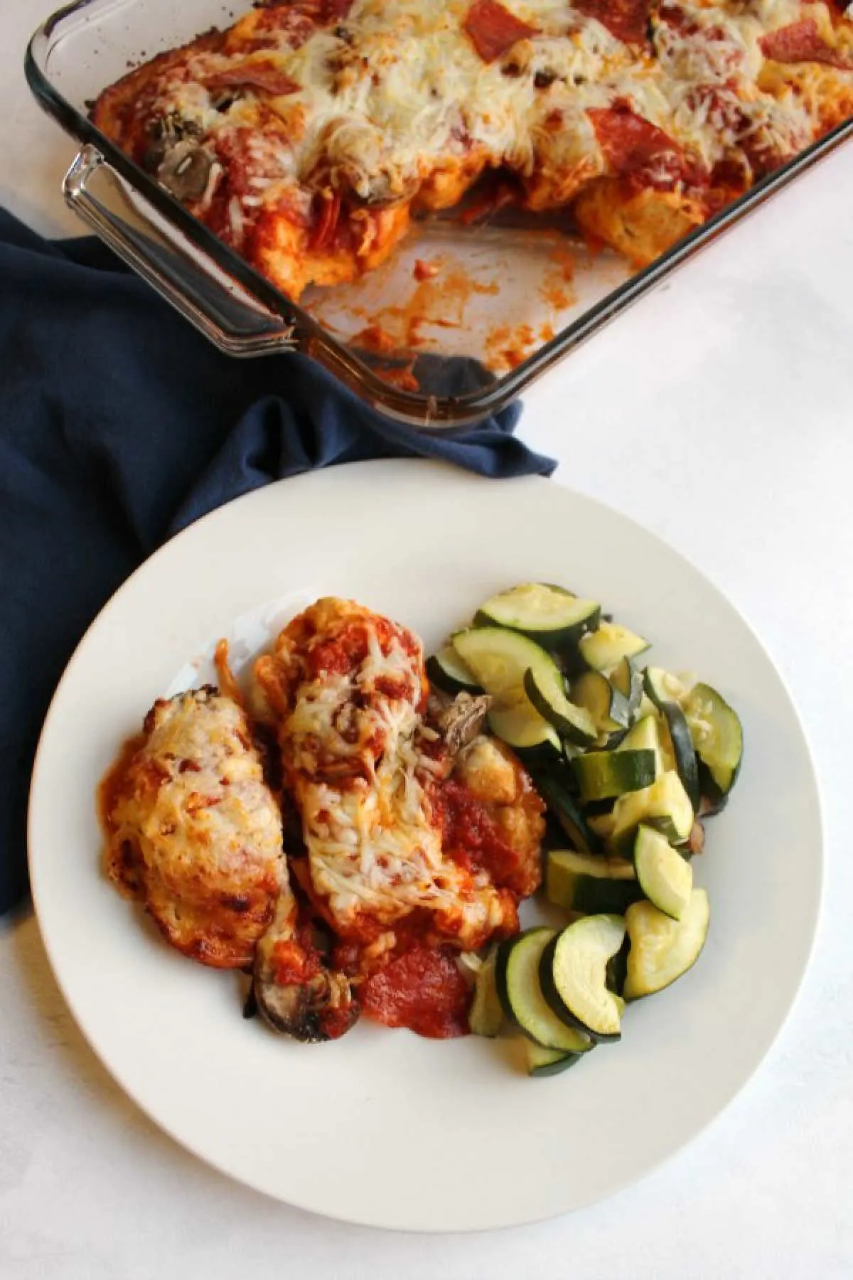 Serving of bubble up pizza casserole on dinner plate with sauteed zucchini, ready to eat.