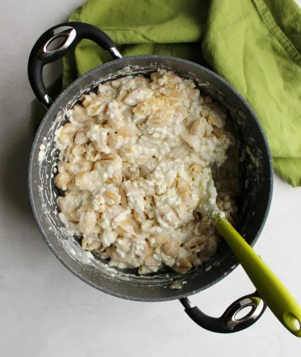 stock pot filled with shell pasta and creamy cottage cheese mixture for casserole.