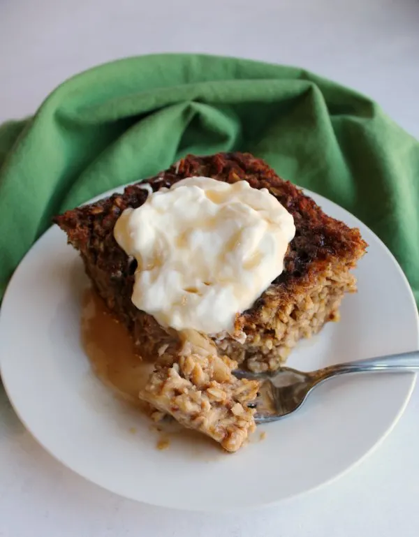 fork of cinnamon banana bread baked oatmeal in front of piece topped with honey and yogurt.