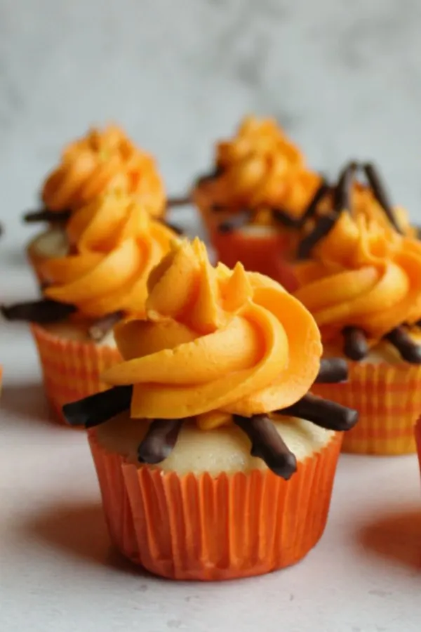 Cupcakes topped with yellow and orange frosting fire and chocolate covered pretzel twigs. 