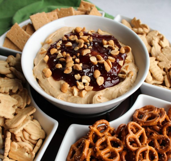 close up of bowl of peanut butter and jelly dip surrounded by animal crackers, pretzels and graham crackers