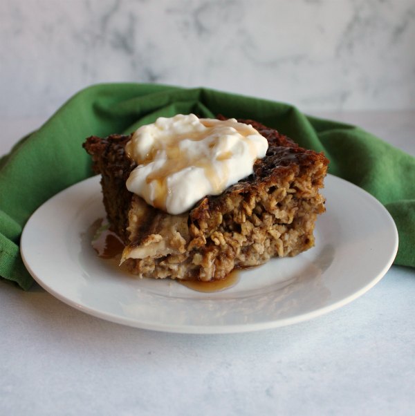 piece of banana bread baked oatmeal served with yogurt and a drizzle of maple syrup.