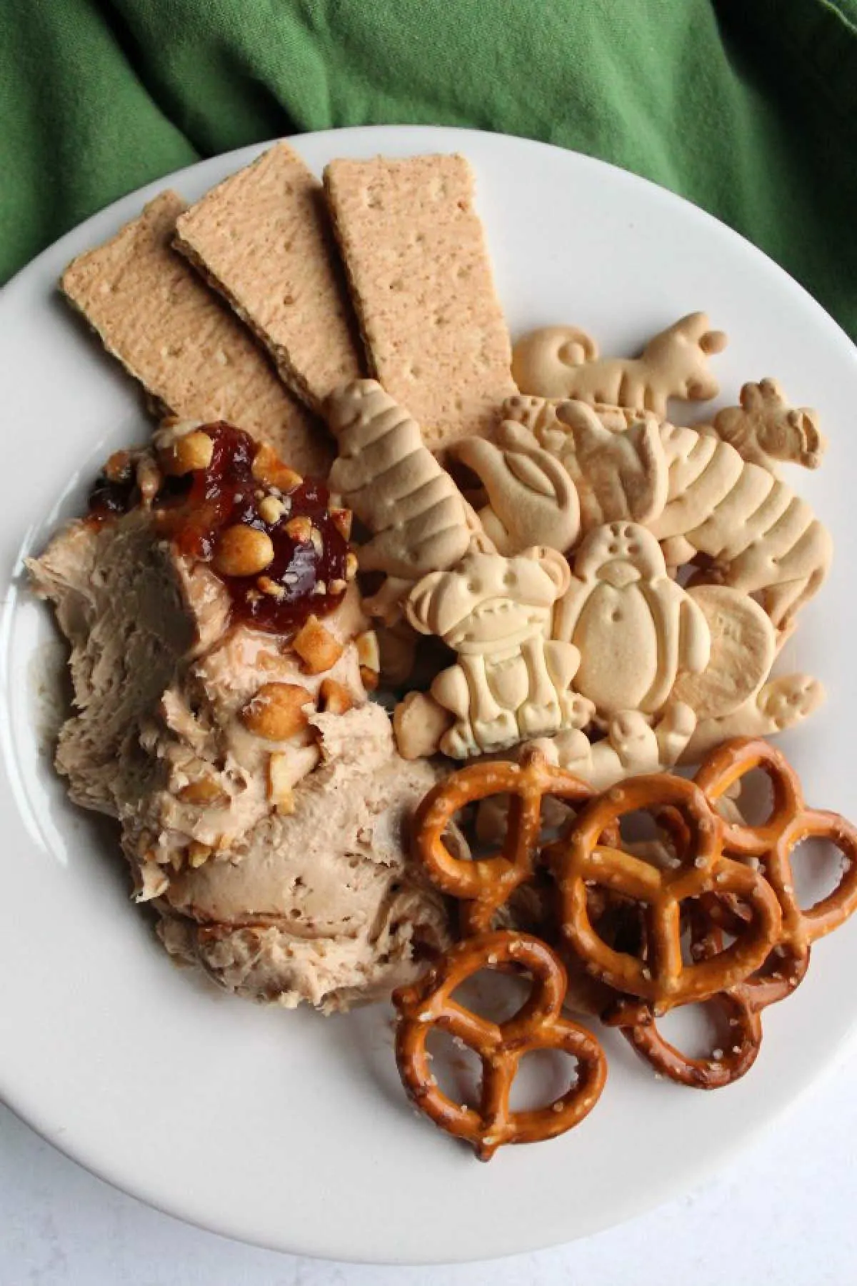 small plate filled with peanut butter and jelly dip, animal crackers, pretzels and graham crackers.