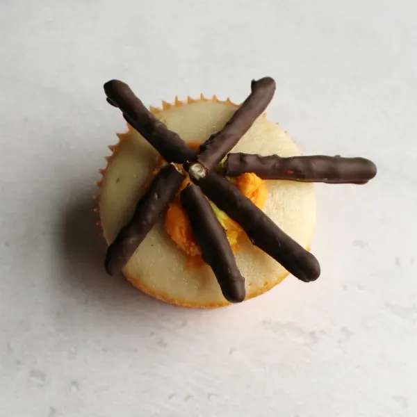cupcake with dollop of frosting in center and chocolate dipped pretzel sticks fanned around.