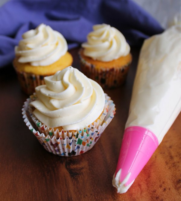 piping bag filled with creamy vanilla russian buttercream next to cupcakes with swirls of frosting on top.