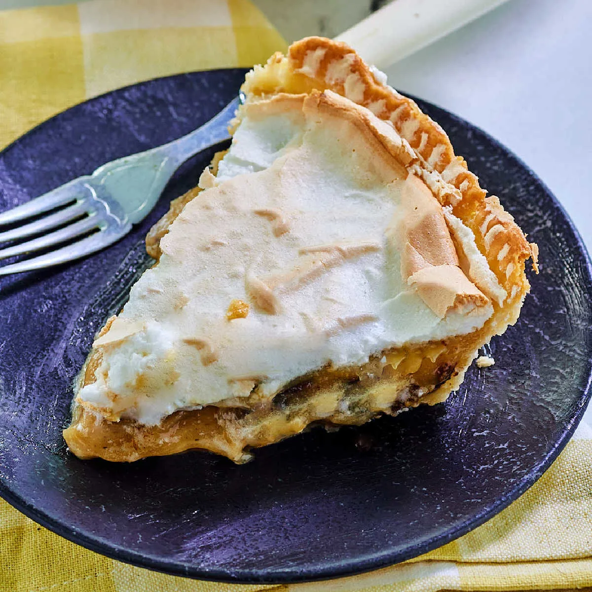 Slice of sour cream raisin pie with meringue on top on small dessert plate with fork, ready to eat.