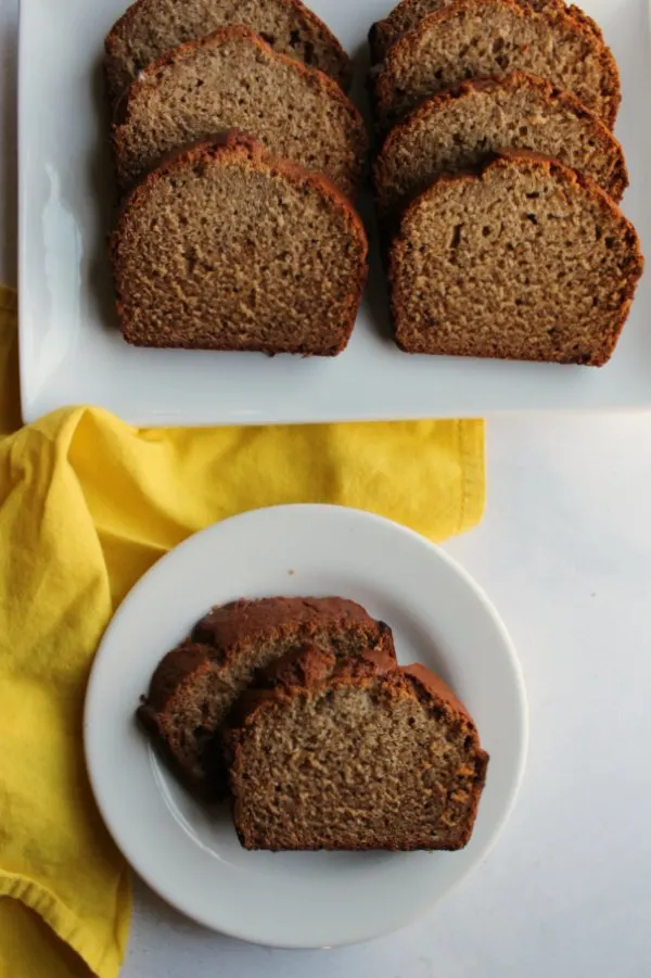 two slices of banana bread served on small plate with platter of slices in background.