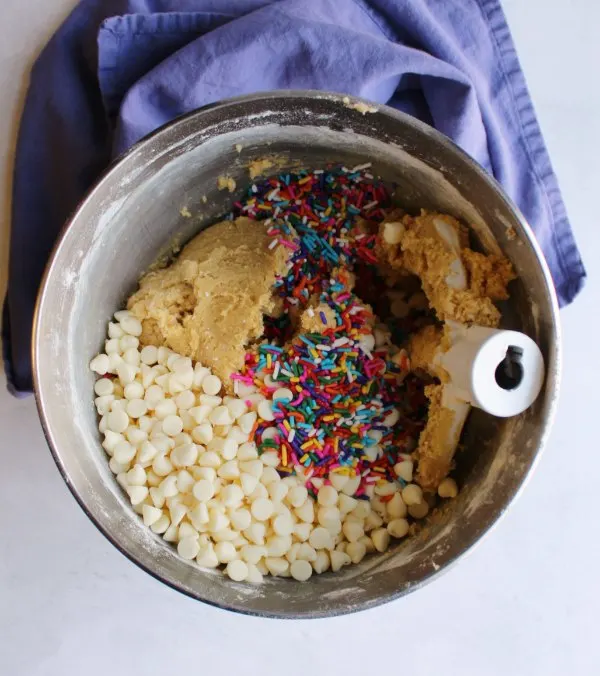 mixing bowl of cookie dough, white chips and sprinkles ready to be mixed together.