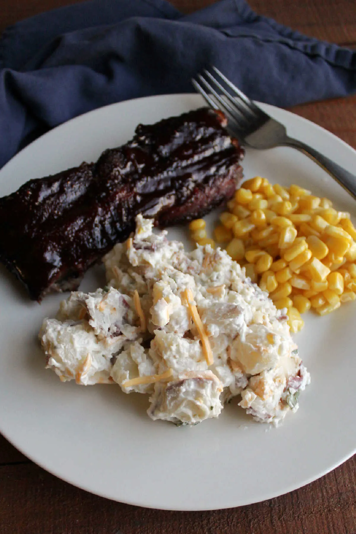 Dinner plate with bacon ranch potato salad, corn, and bbq ribs.