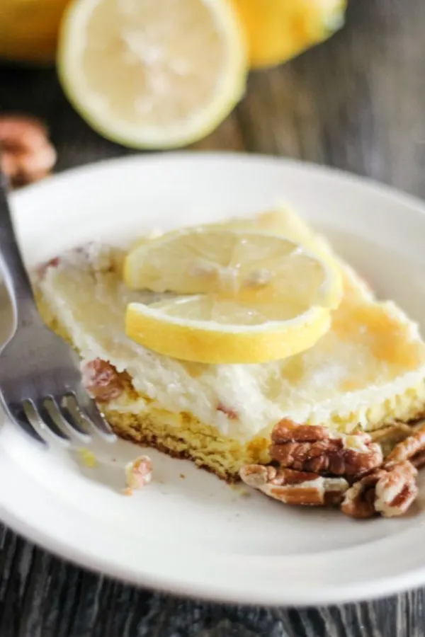 bite missing from square of lemon cake bars with pecans and cream cheese