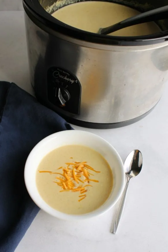 bowl of creamy cheddar broccoli soup next to crock pot of soup