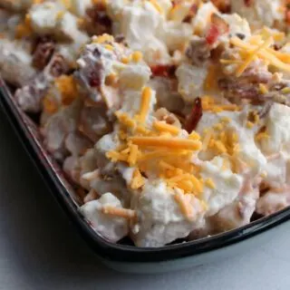 Close up of cheddar bacon ranch potato salad with shreds of orange cheese on creamy potato salad.