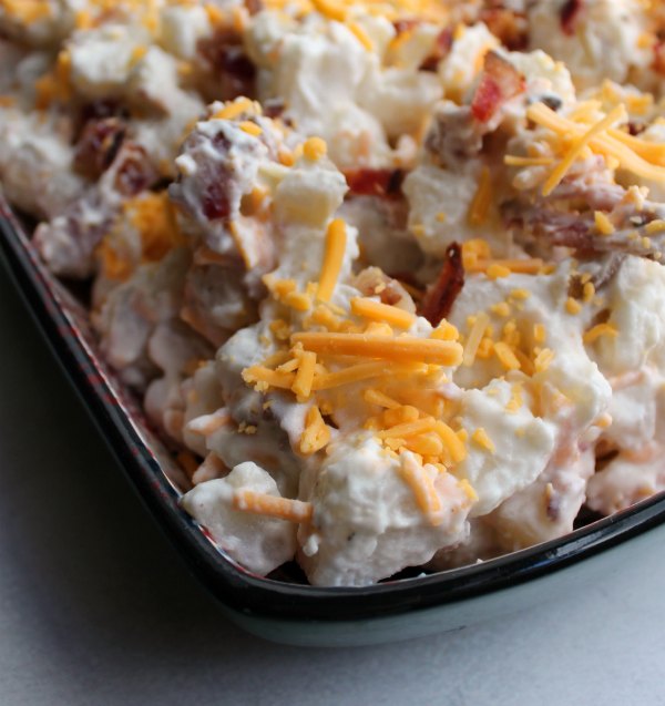 Close up of cheddar bacon ranch potato salad with shreds of orange cheese on creamy potato salad.