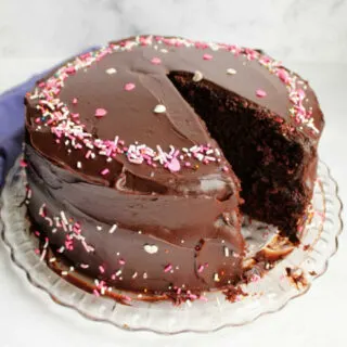 devilishly good chocolate cake with shiny fudge frosting and sprinkles, one slice missing.