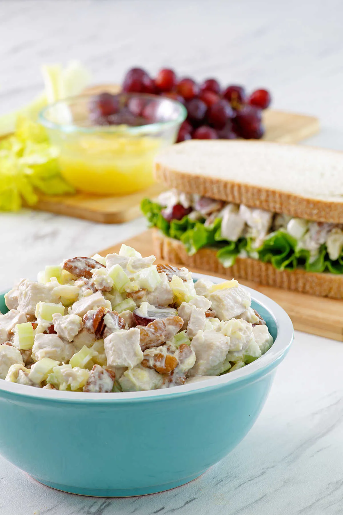 Bowl of fruited chicken salad with sandwich and remaining ingredients in the background.