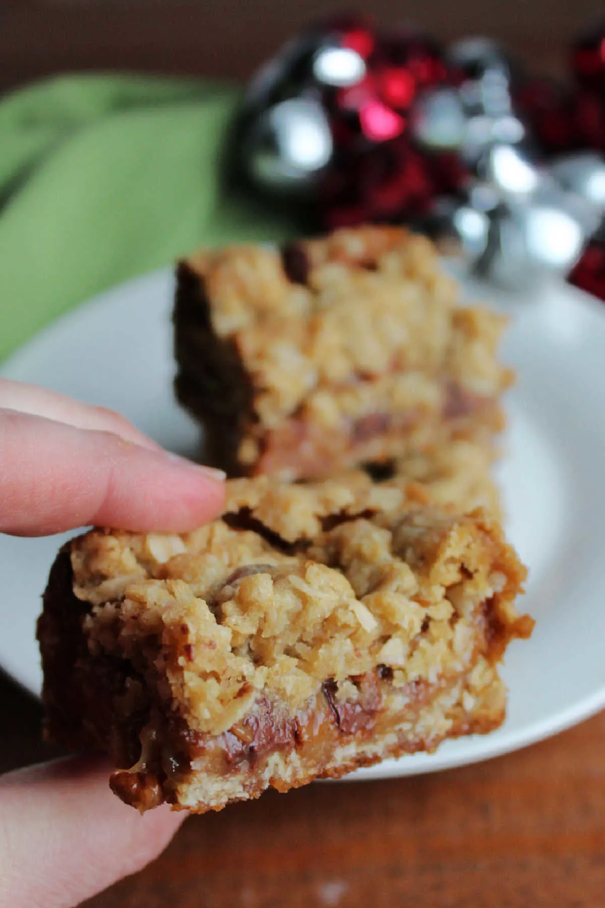 Hand holding oatmeal caramelita bar with gooey caramel, chocolate and pecan center showing.