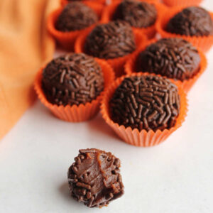 inside of chocolate orange brigadeiro with soft chocolate condensed milk center showing with more sprinkle coated truffles in the background.