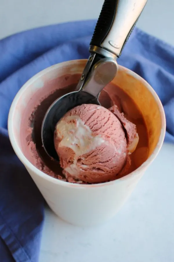 scoop digging into container of pink velvet ice cream.