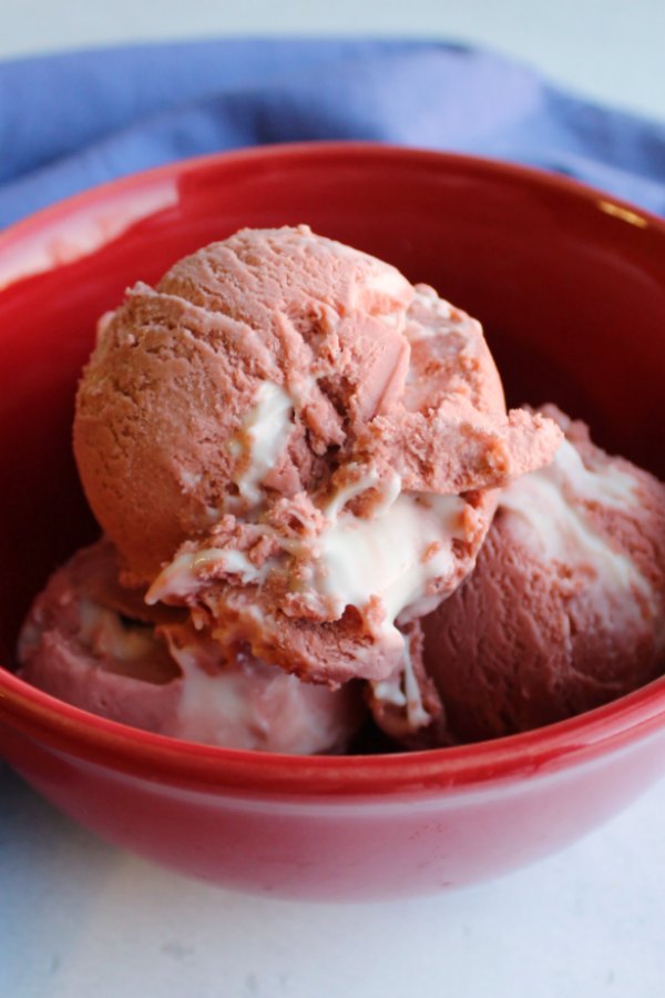 scoops of pink velvet ice cream in red bowl with gooey cream cheese swirl showing