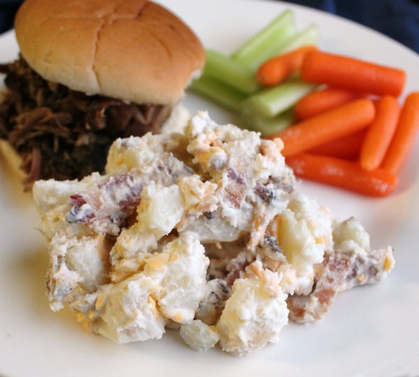 serving of cheddar bacon ranch potato salad on plate with pulled pork sandwich and veggies