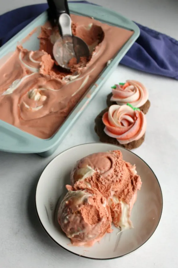 scoops of pink velvet ice cream in front of loaf pan with additional ice cream and two cookies nearby