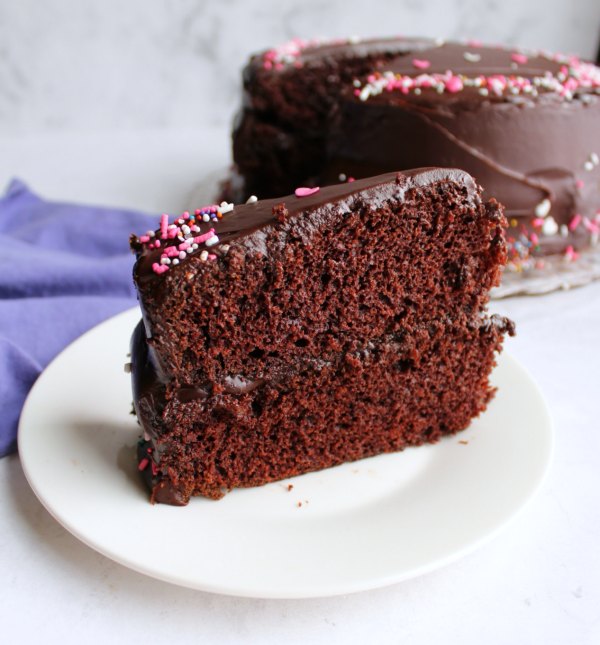 slice of chocolate layer cake with shiny chocolate frosting and sprinkles