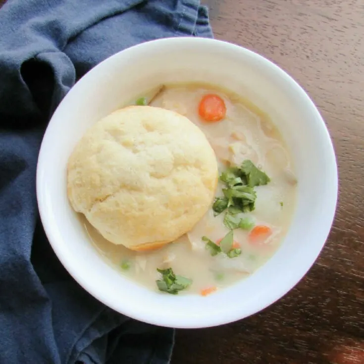 Bowl of creamy chicken pot pie soup topped with fresh herbs and a golden brown biscuit.