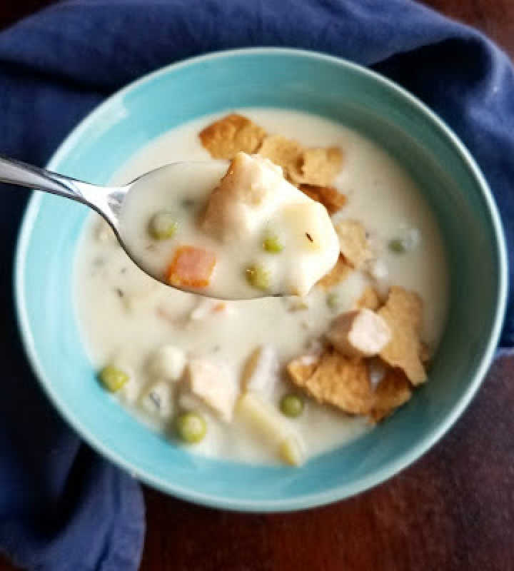Bite of creamy chicken pot pie soup on spoon with bits of crumbled pie crust on top.