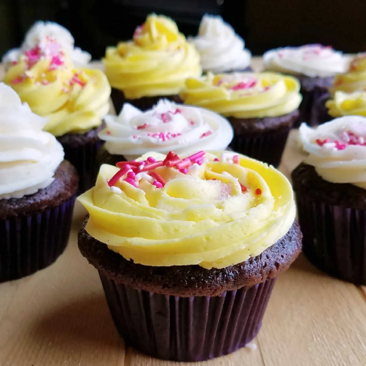 Rich chocolate cupcakes decorated with white and yellow condensed milk buttercream and pink and white sprinkles.