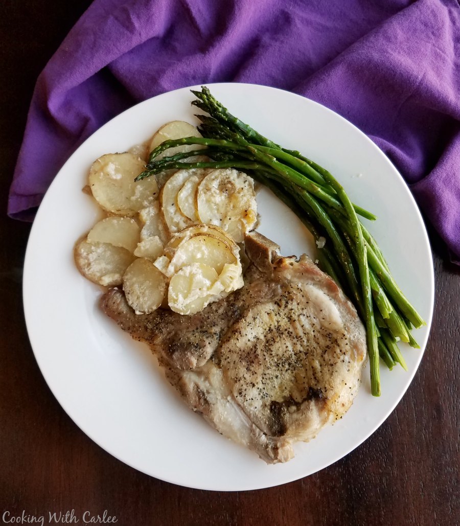 Plate of scalloped potatoes with pork chop and asparagus.