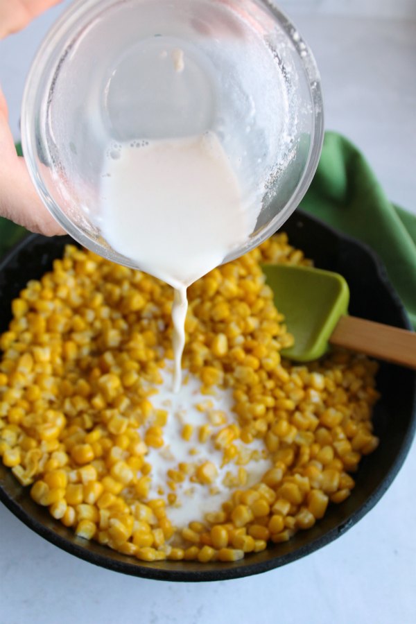 pouring milk mixture over corn in cast iron skillet.