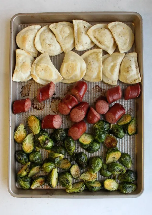 cooked pierogi, hunks of sausage and halved brussels sprouts on sheet pan