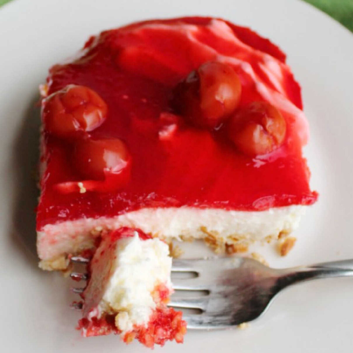 Bite of cherry pretzel salad on fork showing cream cheese center and cherry jello topping.