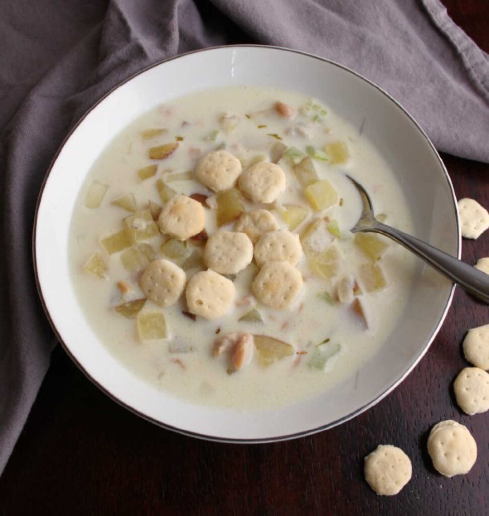 close up of spoon in bowl of creamy clam chowder with oyster crackers
