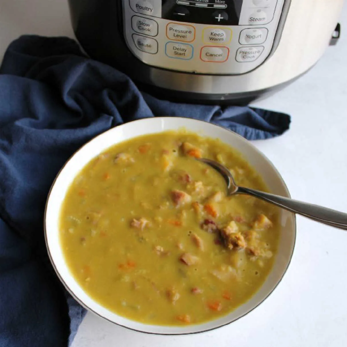 Bowl of thick split pea soup with carrots and ham in front of instant pot it was cooked in.