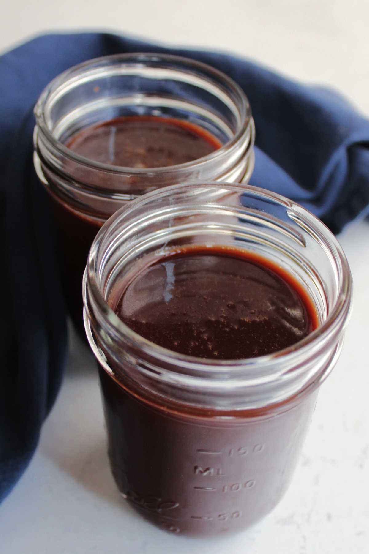 Two glass jars of freshly made hot fudge sauce ready to use.