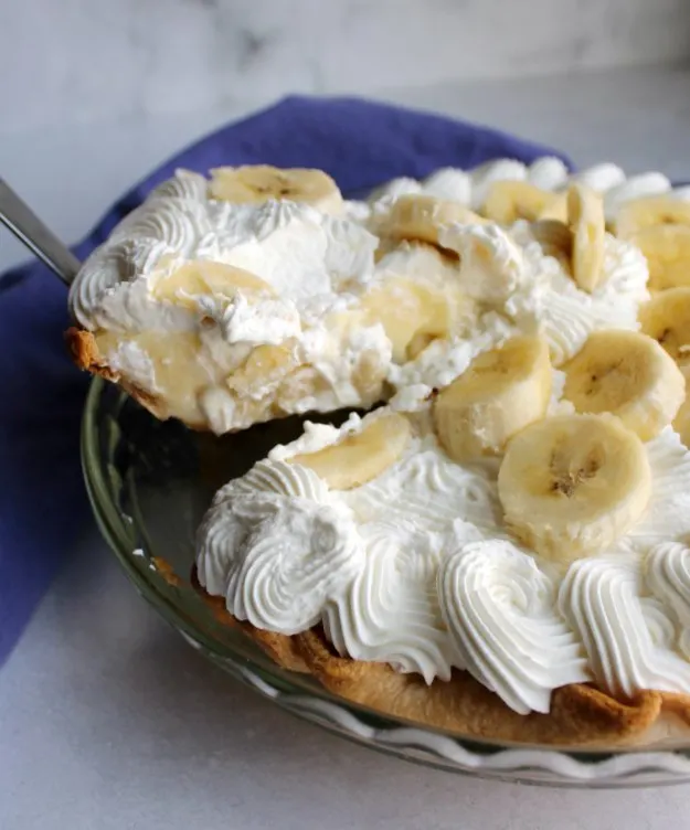 lifting first slice of homemade banana cream pie out of pan.