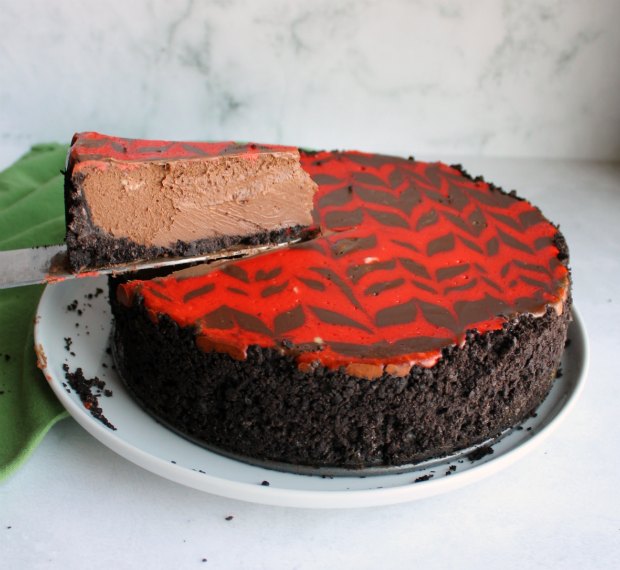 lifting slice of chocolate cheesecake with red pattern out of the whole
