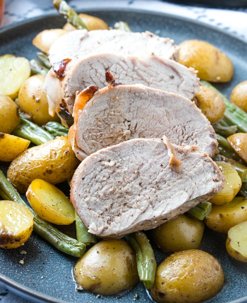 slices of pork tenderloin with green beans and potatoes on plate.