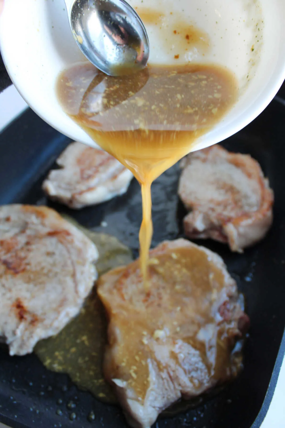 pouring braising liquid over pork chops in electric skillet.