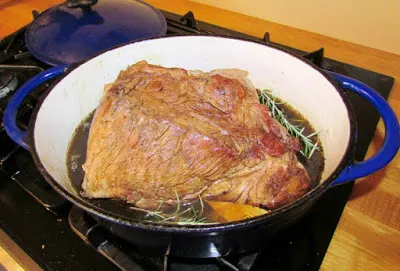 dutch oven with browned pork shoulder in it, ready to braise
